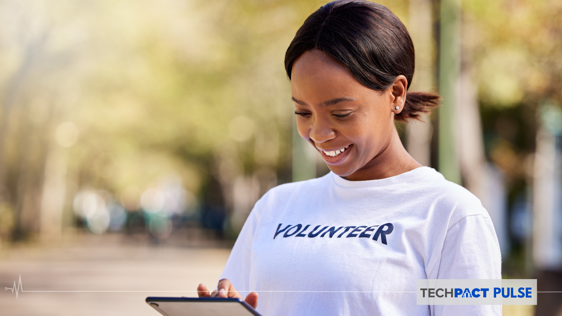 A woman who is outdoor wearing a Volunteer shirt working on a tablet while smiling
