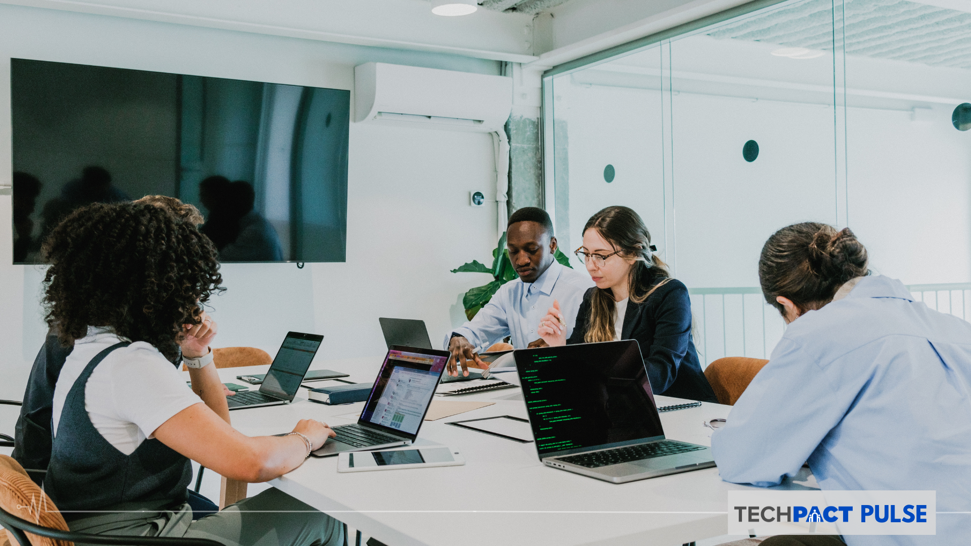 Diverse people working on laptops on a conference table in a professional setting, during the day