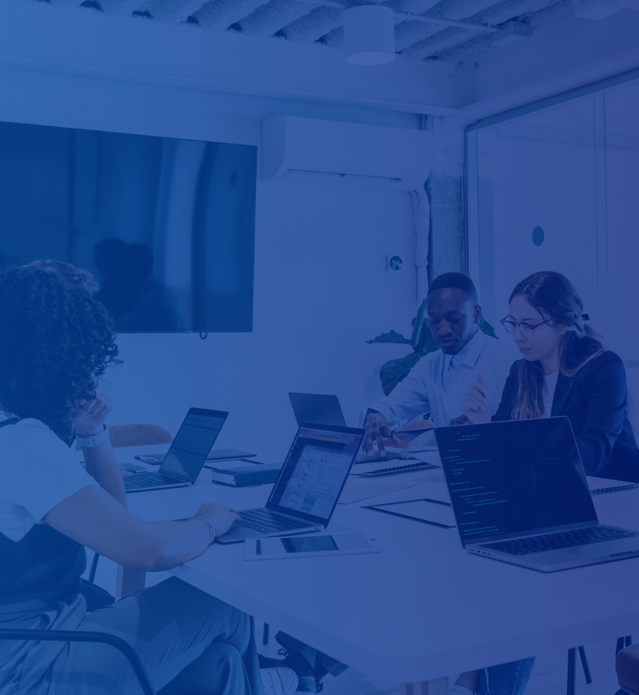A group of diverse people around a desk working with laptops